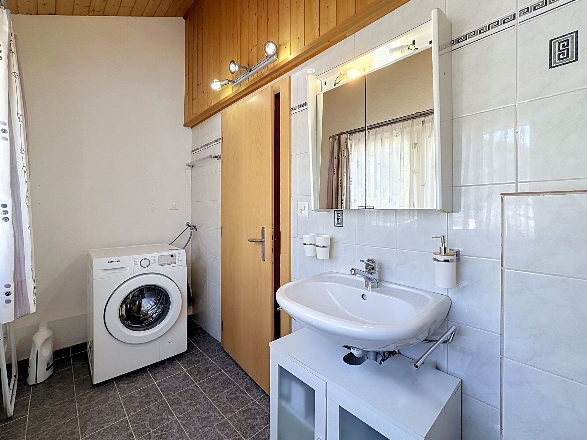 Une petite salle de bain équipée d’un lave-linge, d’un lavabo et d’un miroir.