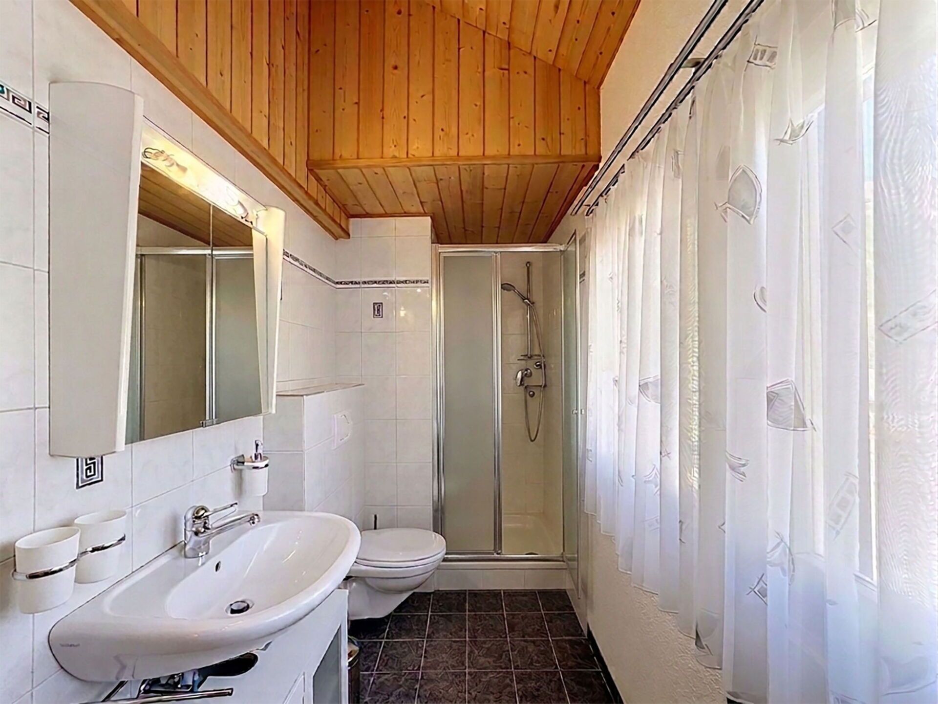 Een badkamer met een houten plafond, een douchecabine, een wastafel en een toilet.