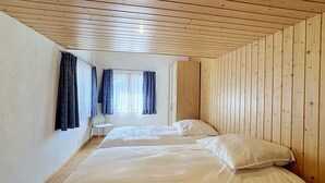 Ein Zimmer mit Holzwandverkleidung, einem Bett mit weißer Bettwäsche, einem Stuhl und einem Fenster mit Vorhängen.