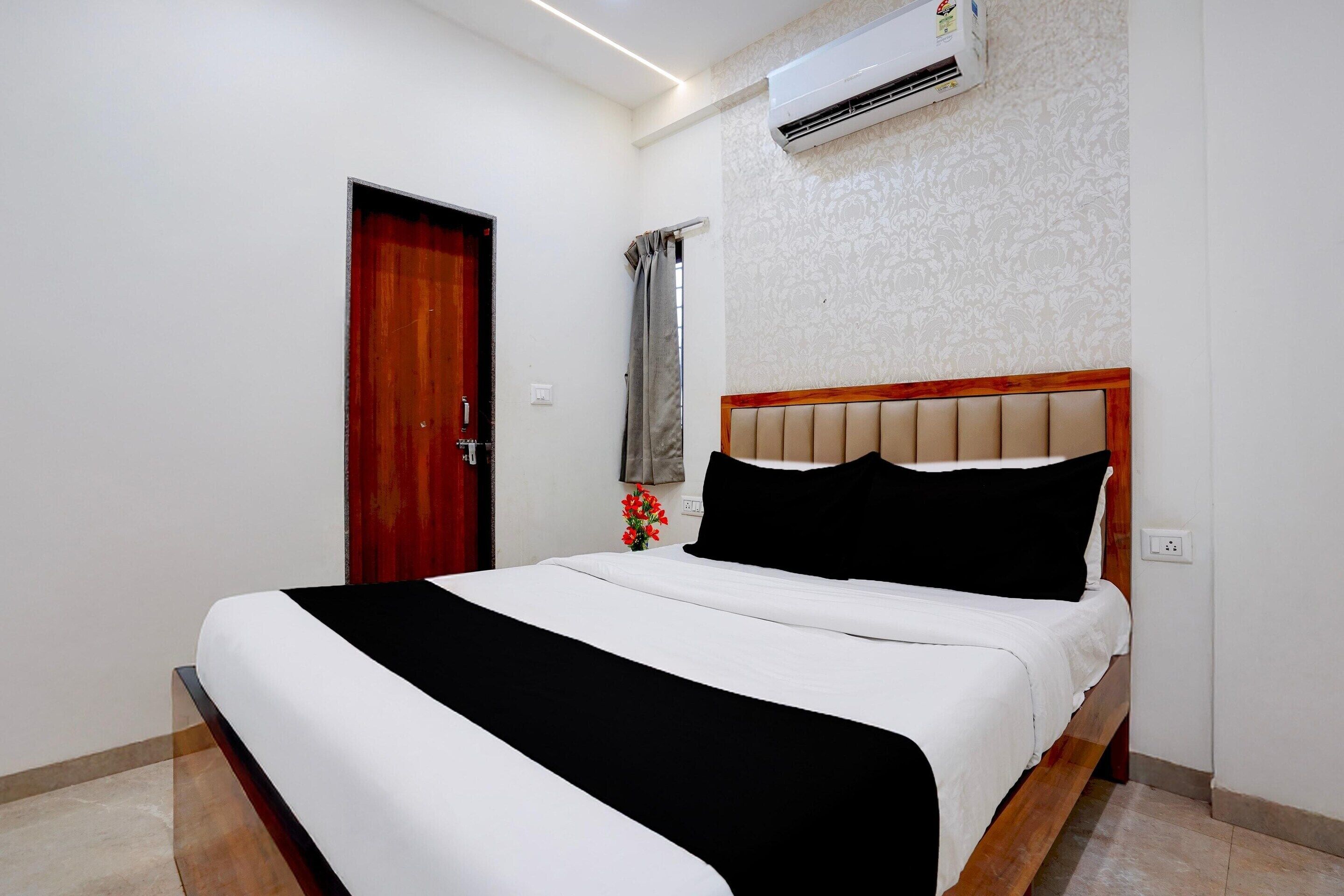 A hotel room with a bed, a window with curtains, an air conditioning unit, and a door.