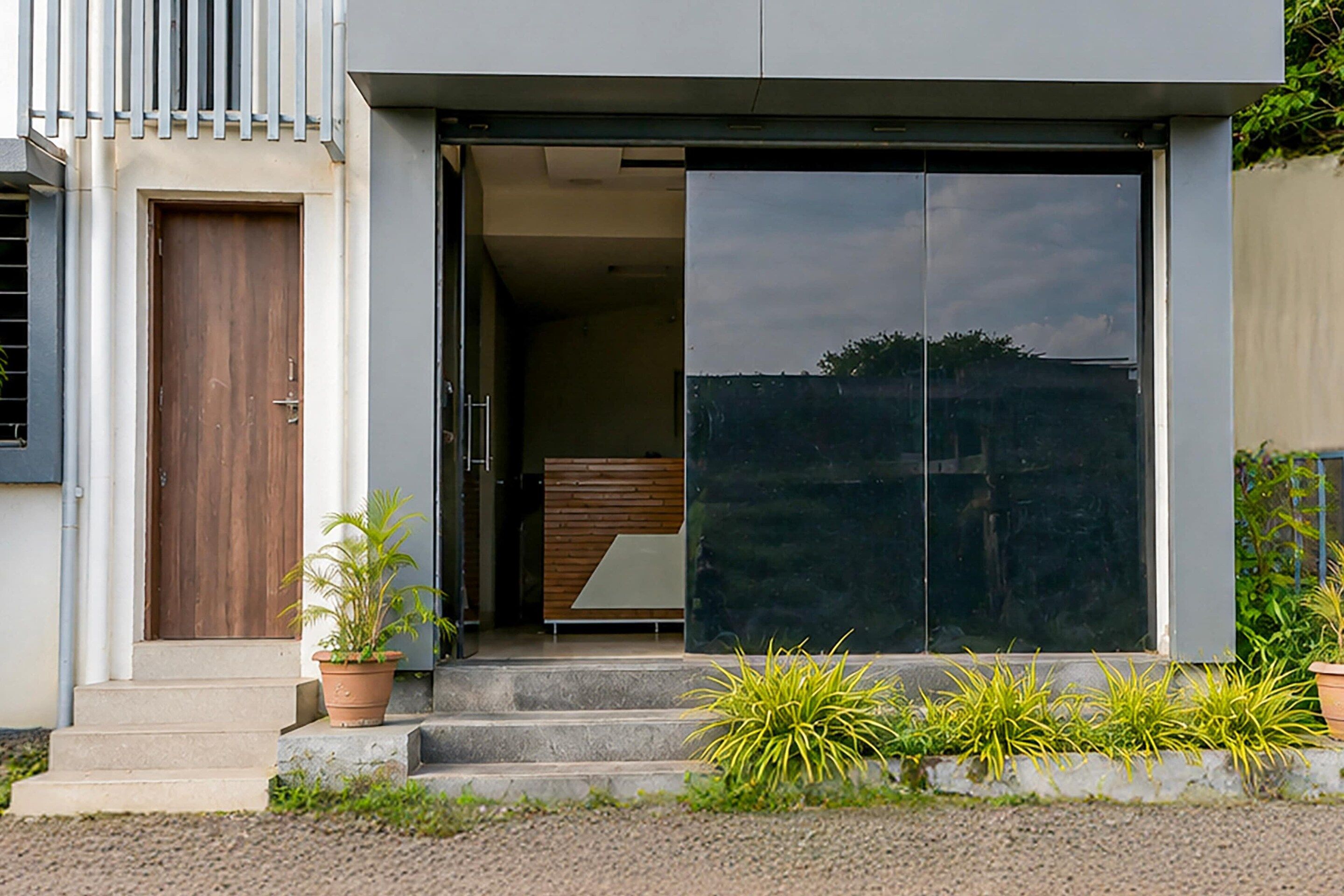 Un bâtiment moderne doté d’une grande entrée avec une porte-fenêtre coulissante, d’une porte en bois sur la gauche et d’un petit escalier menant à la porte.