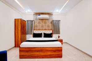 Ein Schlafzimmer mit einem hölzernen Bett, einem Kleiderschrank, einer Klimaanlage und einem Nachttisch mit einer Flasche und Blumen.