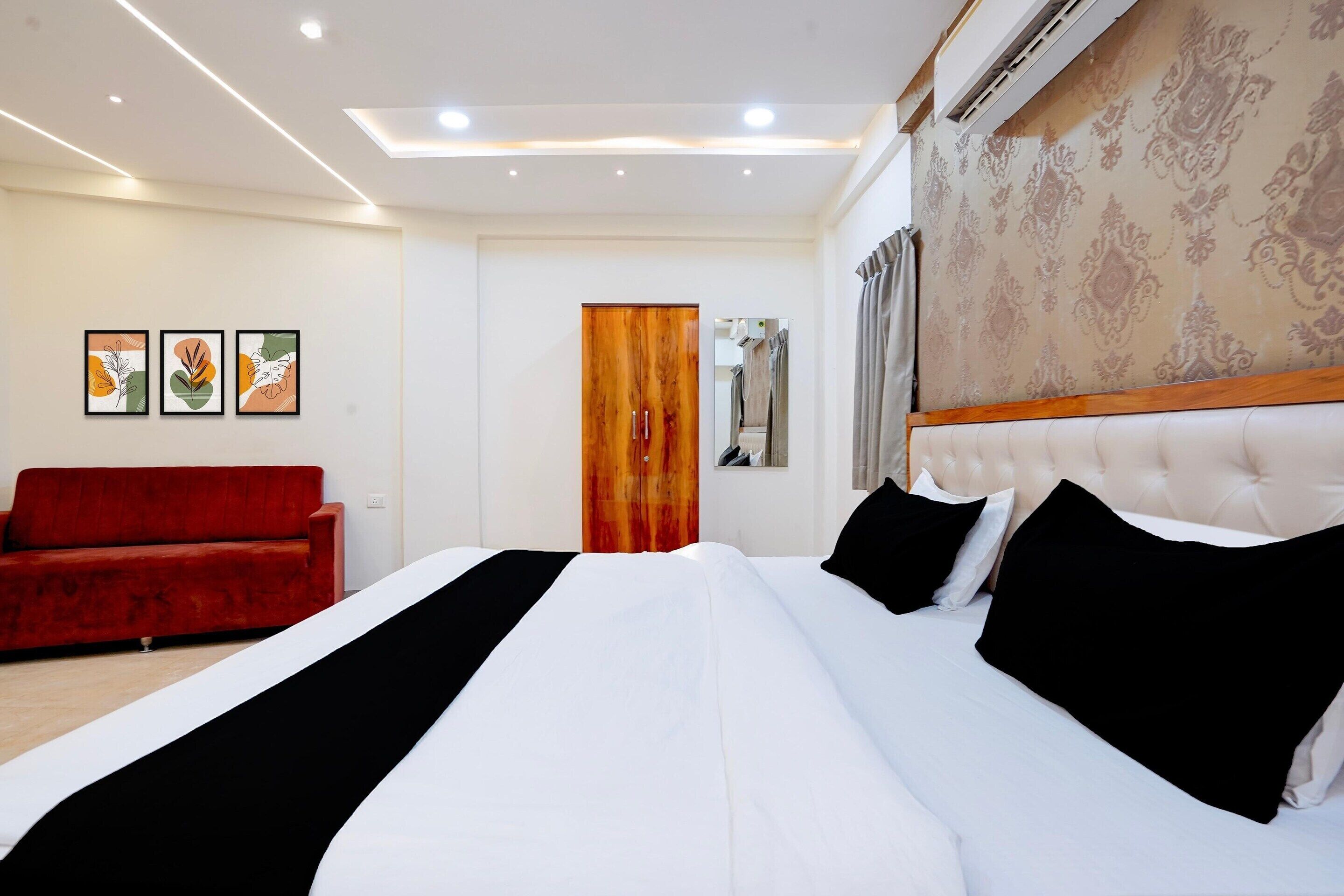 A hotel room with a large bed, a red sofa, and three framed artworks on the wall.