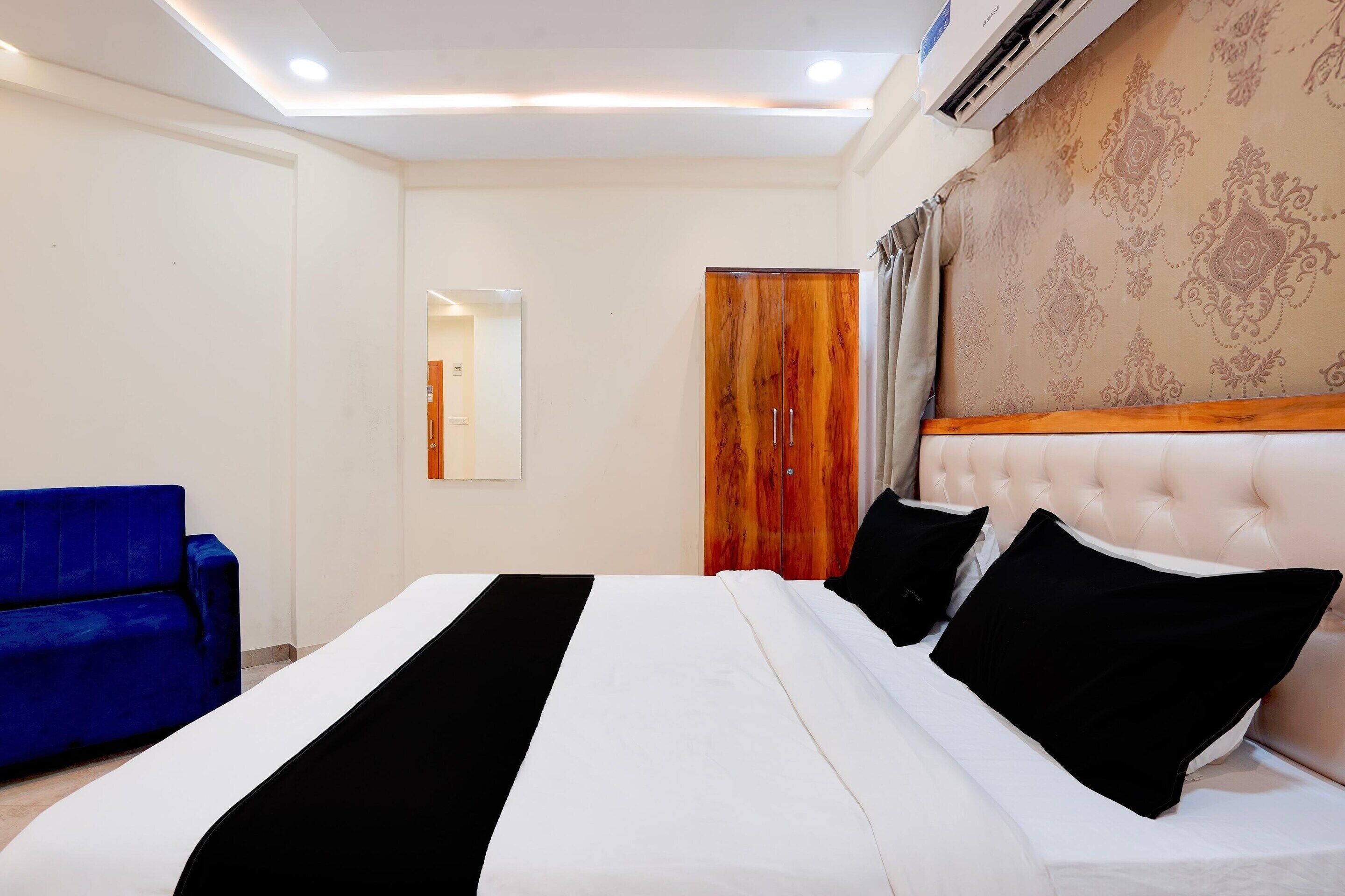 A hotel room with a bed, a blue armchair, a wooden wardrobe, and a patterned wallpaper.
