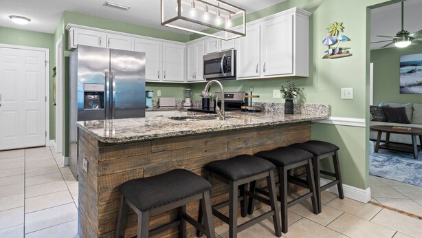 A kitchen with white cabinets, a stainless steel refrigerator, a microwave, and a granite countertop. - Coastal Orange Beach Retreat Minutes to the Beach, The Wharf & Family Fun (Orange Beach)