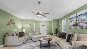 A living room with a ceiling fan, green walls, and a large painting. - Coastal Orange Beach Retreat Minutes to the Beach, The Wharf & Family Fun (Orange Beach)