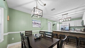 A dining area with a wooden table and chairs, a kitchen with stainless steel appliances, and a hanging light fixture. - Coastal Orange Beach Retreat Minutes to the Beach, The Wharf & Family Fun (Orange Beach)