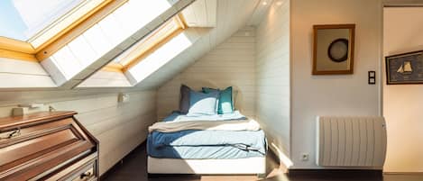 A bedroom with a skylight, a bed with pillows, a dresser, and a radiator.