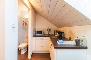 Una cocina compacta con microondas, cafetera y un lavamanos pequeño.