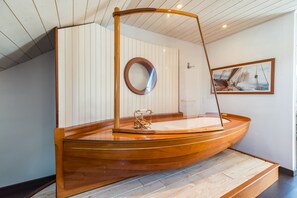 A wooden boat-shaped bathtub with a glass enclosure, a wooden floor, and a framed picture on the wall. - Au Chemin des Amoureux - Maison cosy pour 2 (Lannion)