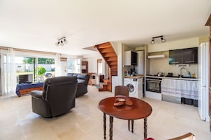 Amplia sala de estar con sofá, mesa de comedor y cocina equipada con lavadora y horno.