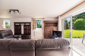 A living room with a sofa set, a television, and a view of the outdoors. - Au Chemin des Amoureux - Maison cosy pour 2 (Lannion)