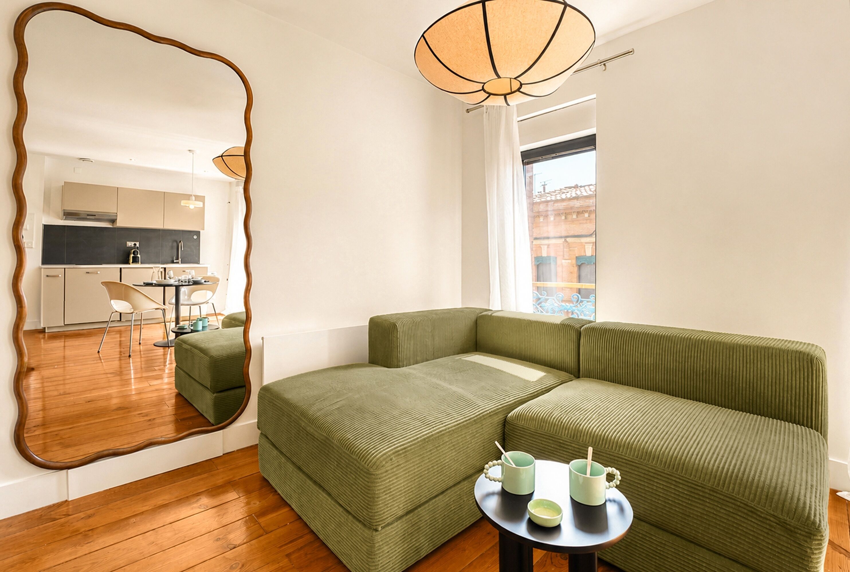 Una sala de estar moderna con un sofá verde, una mesa redonda con tazas, y un espejo grande que refleja la habitación.