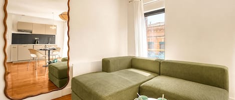 A modern living room with a green sofa, a round table with cups, and a large mirror reflecting the room.