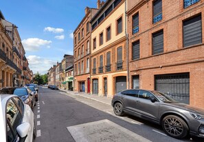 Un carrer amb edificis d'àmbit elevat, cotxes aparcats i cel serè.