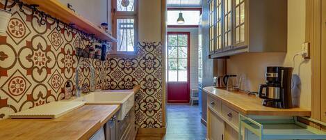 Una cocina estrecha con baldosas estampadas, encimera de madera, lavavajillas Siemens y cafetera.