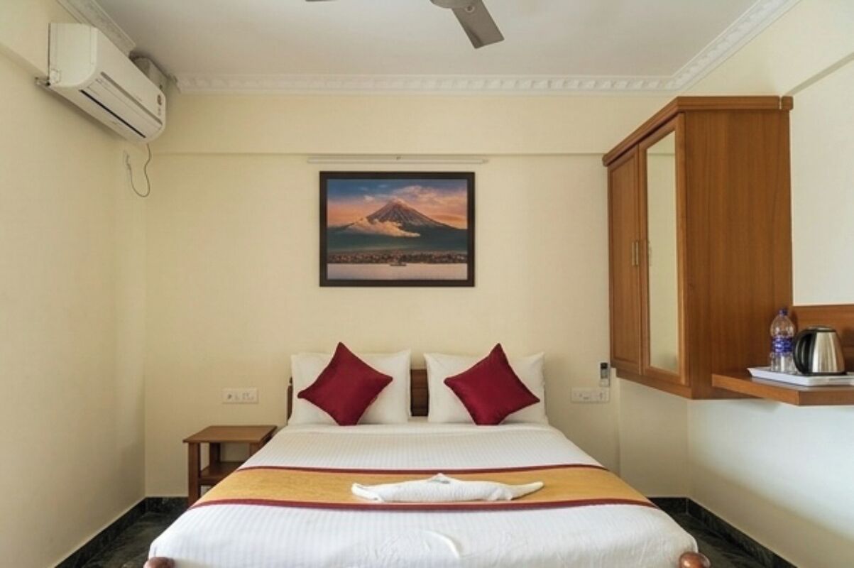 Een hotelkamer met een bed, een nachtkastje, een wandairconditioner, een lijst met een bergfoto en een houten kast.