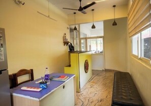 Una habitación de hotel con escritorio, banca, ventilador de techo y ventana.