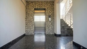 A modern elevator with a textured wall, a marble staircase, and a clean, reflective floor. - Hotel Poptavern Townbridge (Thiruvananthapuram)
