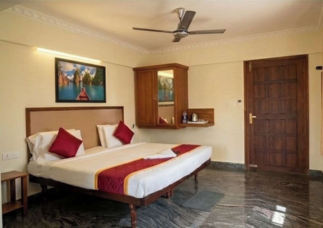 Een hotelkamer met een bed, een plafondventilator, een schilderij, een houten kast en een deur.