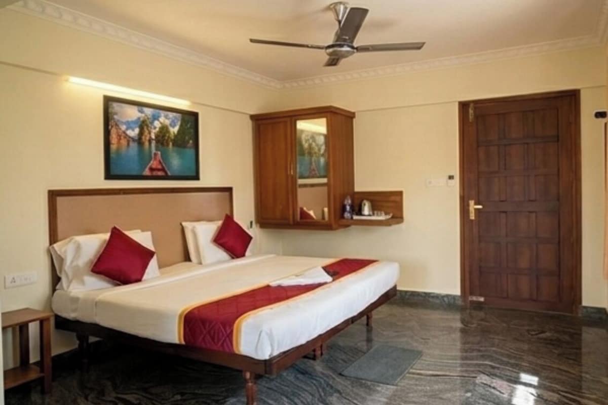 Una habitación de hotel con una cama, un ventilador de techo, un cuadro, un armario de madera y una puerta.