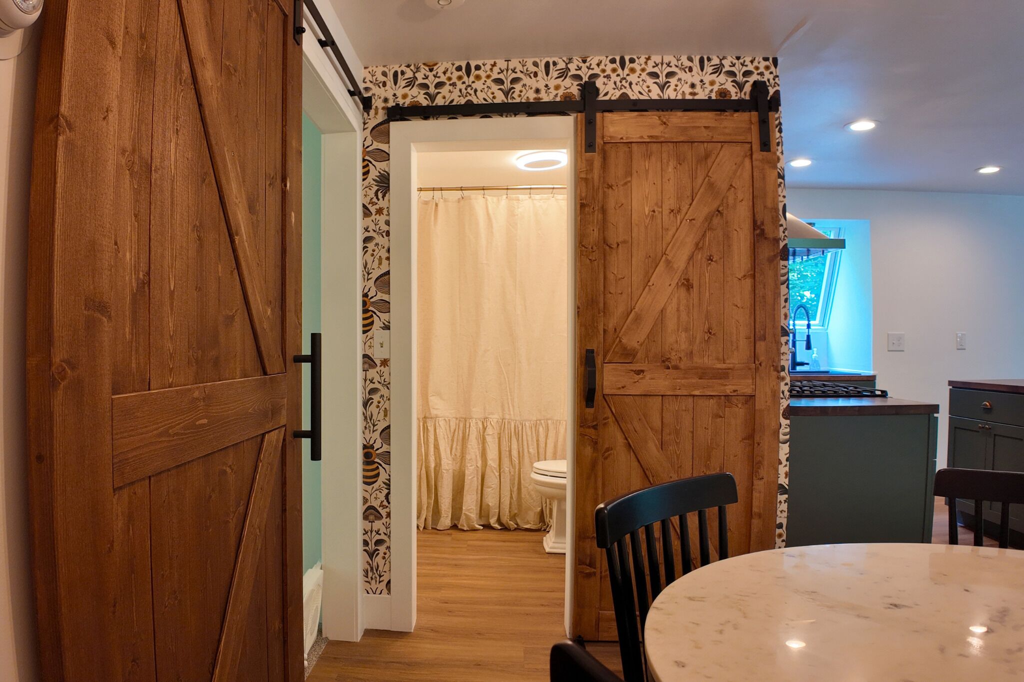Une pièce avec une porte en bois, une table à manger, des chaises, un coin cuisine et une salle de bain équipée de toilettes et d’un rideau de douche.