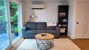 Een woonkamer met een grijze bank, een ronde salontafel, een boekenkast en een airconditioning.