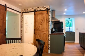 A kitchen with a wooden door, a dining table with chairs, and a view of the outdoors.