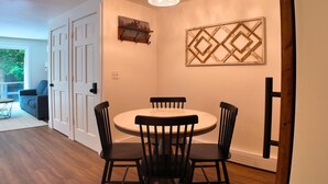 Een eethoek met een ronde tafel en vier stoelen, een hanglamp en een decoratief wandobject.