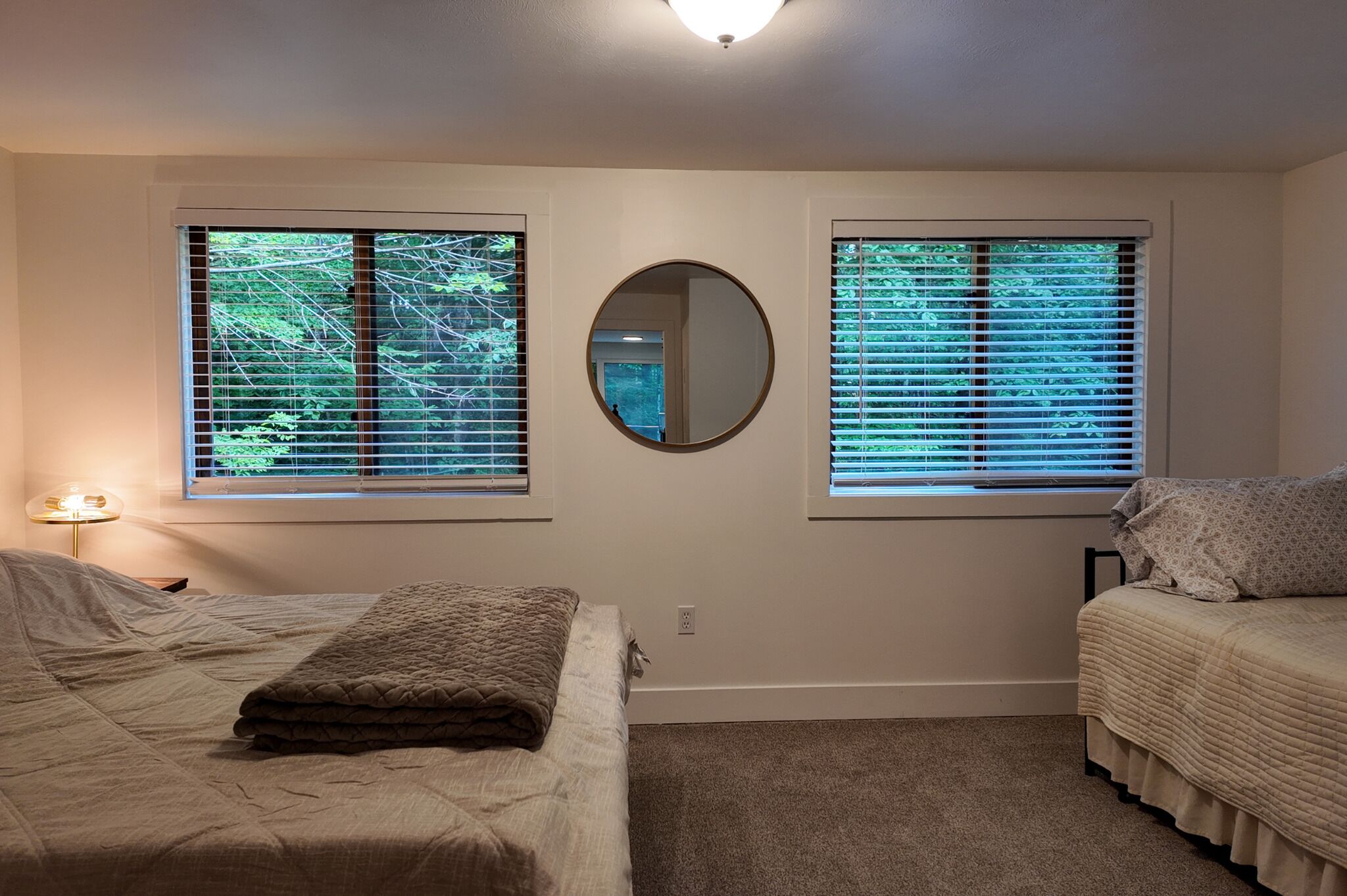 Une chambre avec deux lits, un miroir rond et des fenêtres équipées de stores.