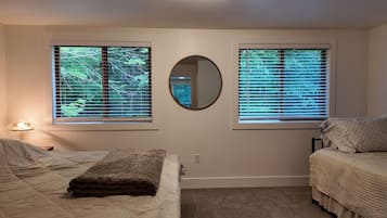 Une chambre avec deux lits, un miroir rond et des fenêtres équipées de stores.