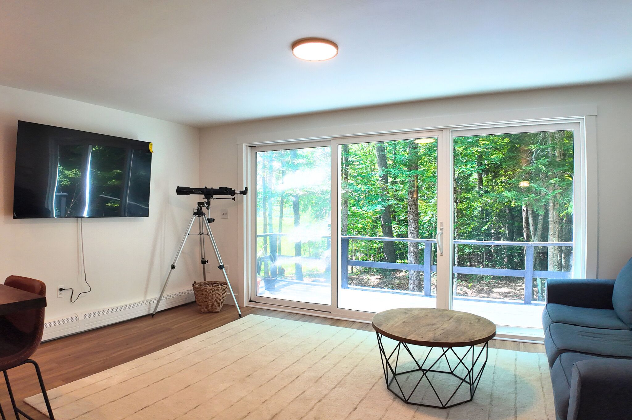 A living room with a telescope, a flat-screen TV, a large window, and a round table.