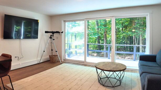 Een woonkamer met een telescoop, een flatscreen televisie, een groot raam en een ronde tafel.