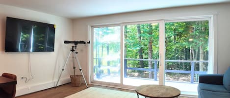 A living room with a telescope, a flat-screen TV, a large window, and a round table.