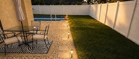 Un patio trasero con piscina, muebles de jardín y una cerca blanca.