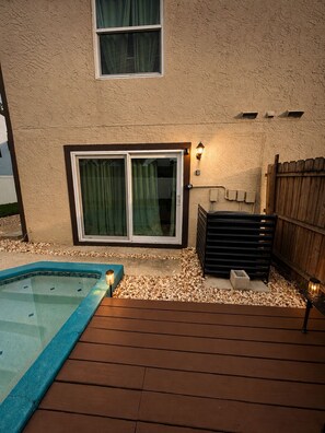 A backyard with a swimming pool, wooden deck, and a covered patio area.