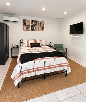 Ein Schlafzimmer mit einem Bett, einem Fernseher, einem Sessel und Kunstwerken an der Wand.