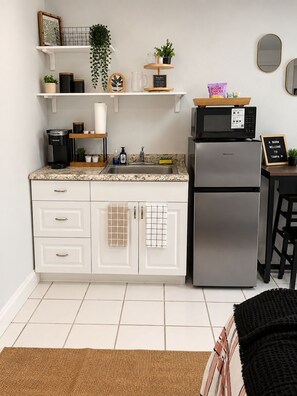 Eine kompakte Küche mit weißen Schränken, einem Edelstahlkühlschrank, einer Kaffeemaschine und einer Mikrowelle auf der Arbeitsfläche.
