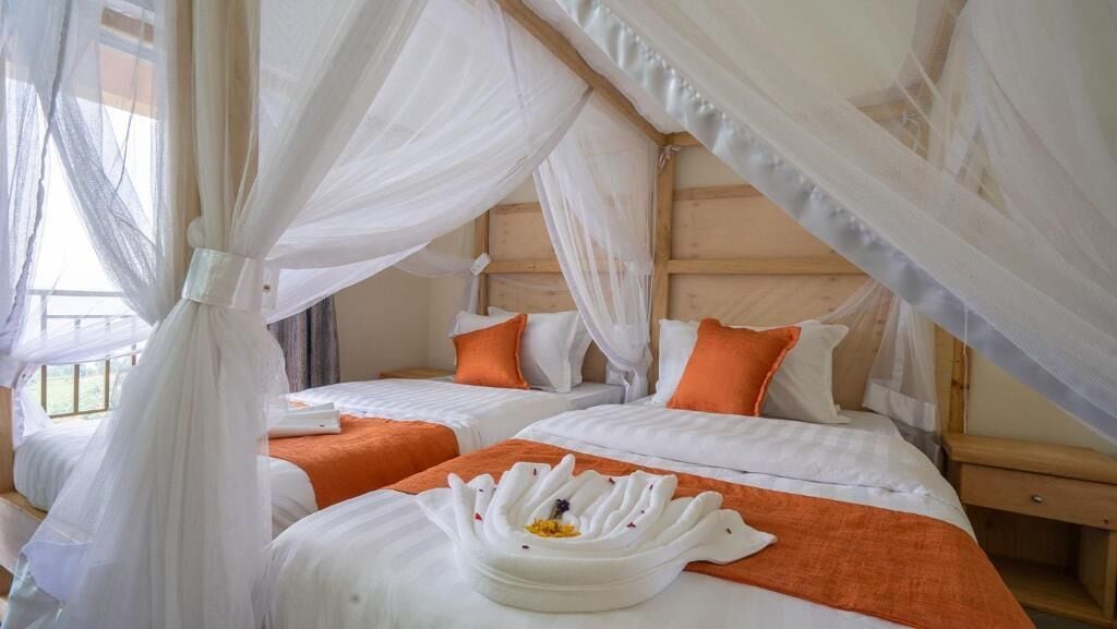 Une chambre avec deux lits, chacun agrémenté de draps blancs et d’oreillers orange, sous un dais.