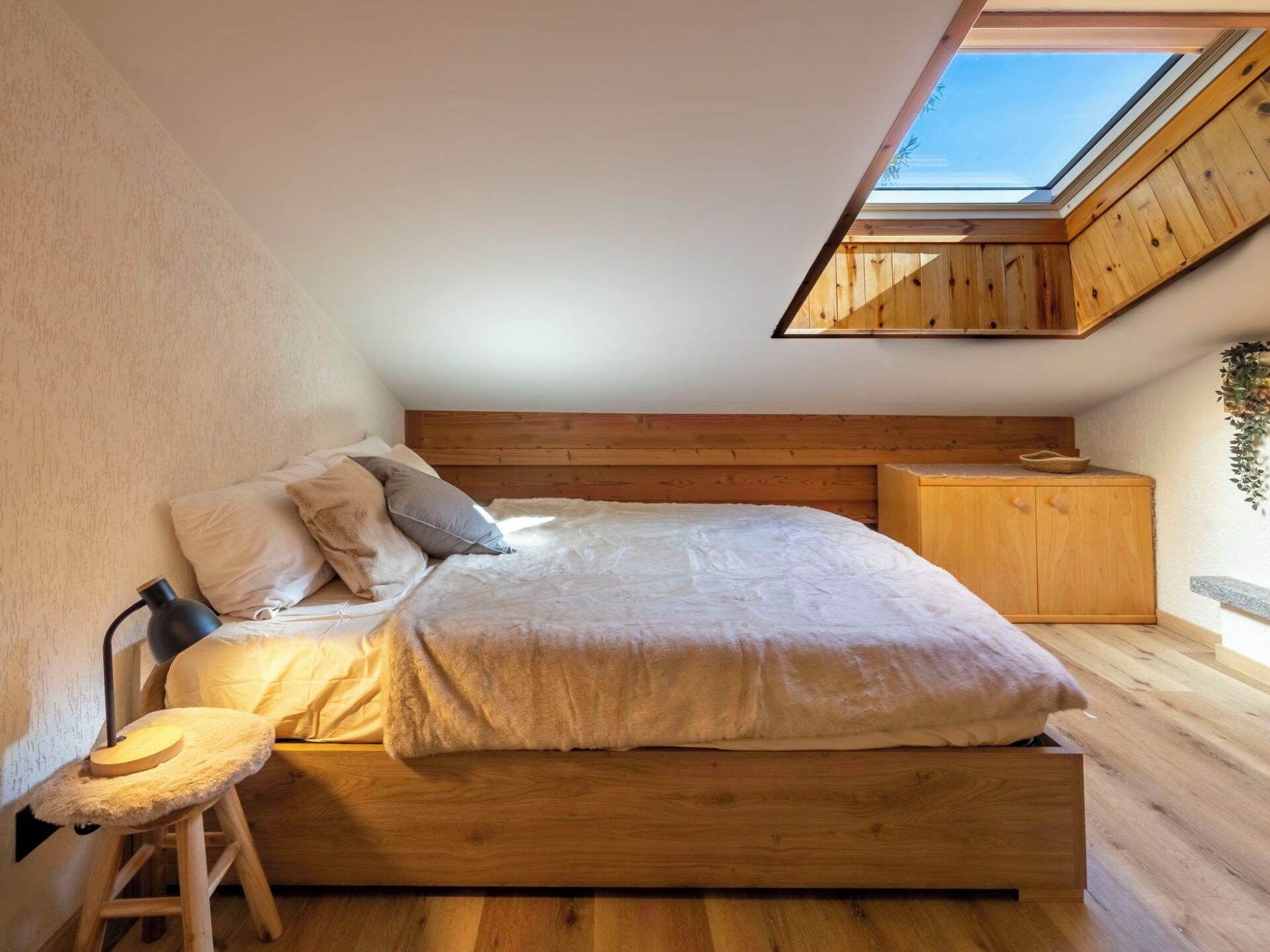 Une chambre avec un puits de lumière, un lit en bois et une table de chevet.