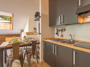 Eine moderne Küche mit Holzarbeitsplatte, Edelstahlspüle und grauen Schränken. Es gibt eine Essecke mit einem Tisch für zwei Personen und Stühlen.