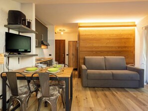 Ein kompakter Wohnraum mit Essbereich, einer Couch, einem Fernseher und einer Holzwand.