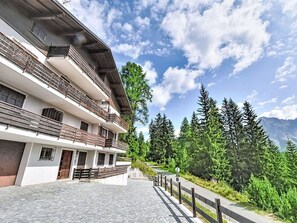A multi-story building with balconies, a paved walkway, and a mountainous backdrop. - Nice apartment for 3 people with WIFI, TV, terrace and pets allowed (Cepina)