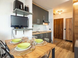 Et moderne køkken med et fladskærms-TV, et træspisebord dækket til fire personer, og en trædør der fører til et andet rum.