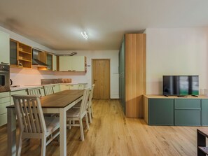Cuina moderna amb armaris de fusta, una taula de dinar amb caires, forn encastrat i un televisor sobre un moble.