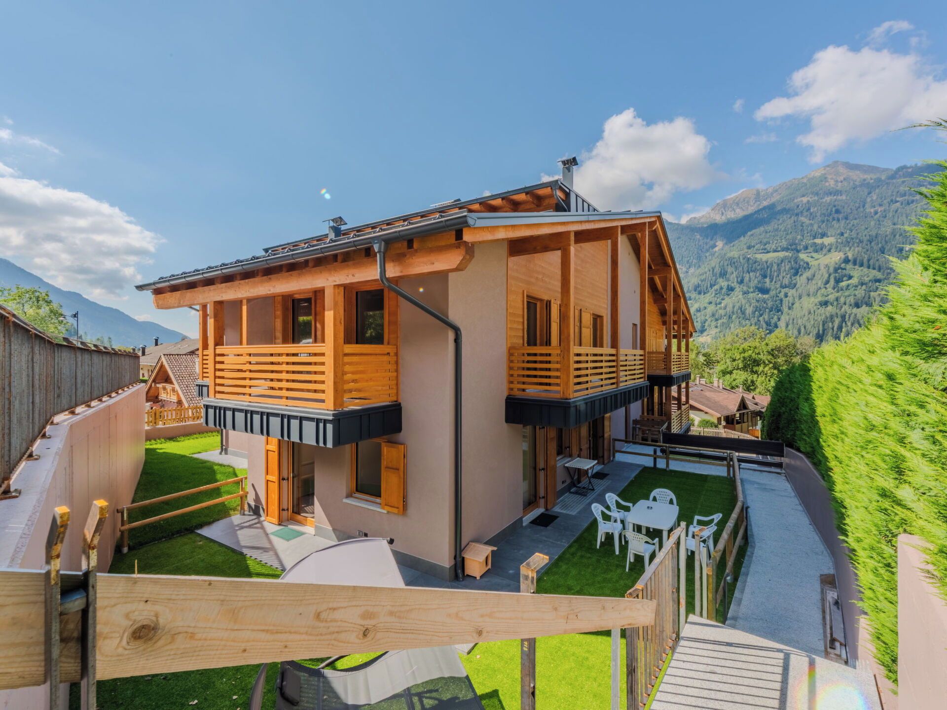Un chalet en bois à deux étages, doté d’un balcon, d’une petite terrasse avec mobilier d’extérieur et offrant une vue sur un paysage montagneux.