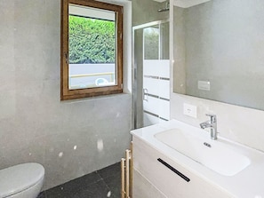 Une salle de bain avec des toilettes, un lavabo et une fenêtre donnant sur un espace verdoyant.
