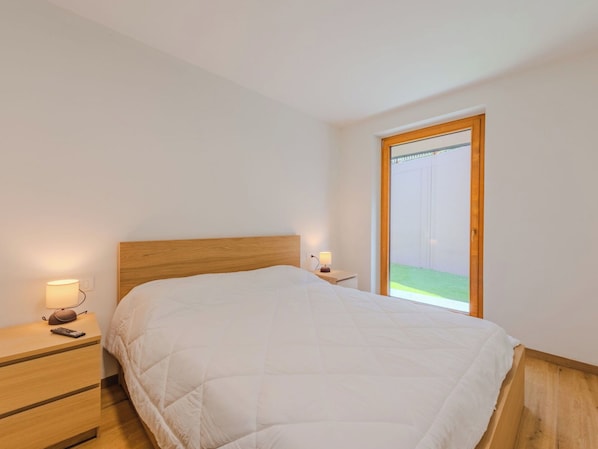 A bedroom with a bed, bedside tables, lamps, and a window with a view of a grassy area.