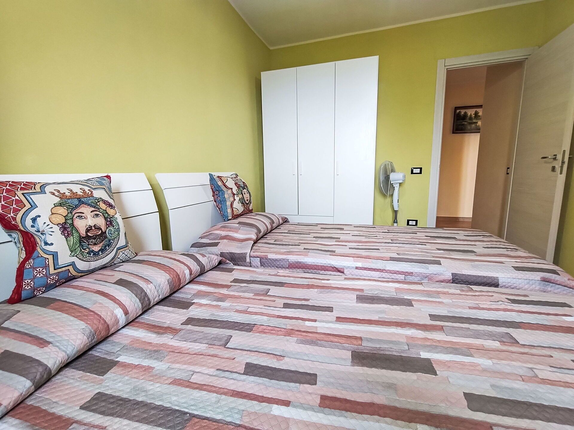 Quarto com cama, guarda-roupa e porta que dá para outro cômodo.