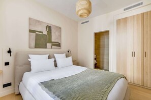A bedroom with a bed, a wall-mounted abstract painting, a woven light fixture, and a wooden wardrobe. - Gorgeous Air-conditioned 2-BR/2Ba  - Saint-Germain (Paris)